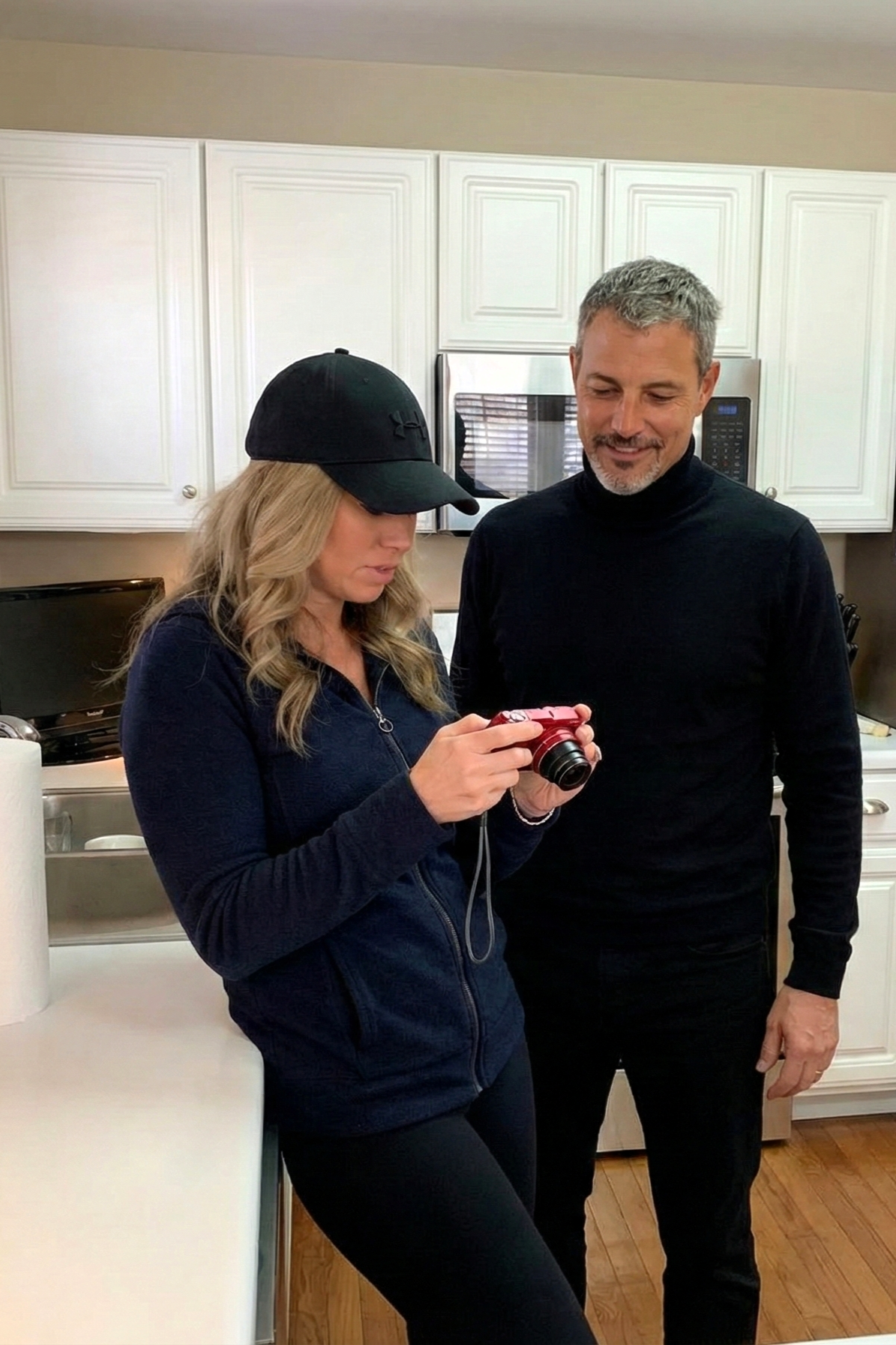 Heather Killebrew showing Joey Montes photos on a red digital camera while standing in a white kitchen in Wildwood.