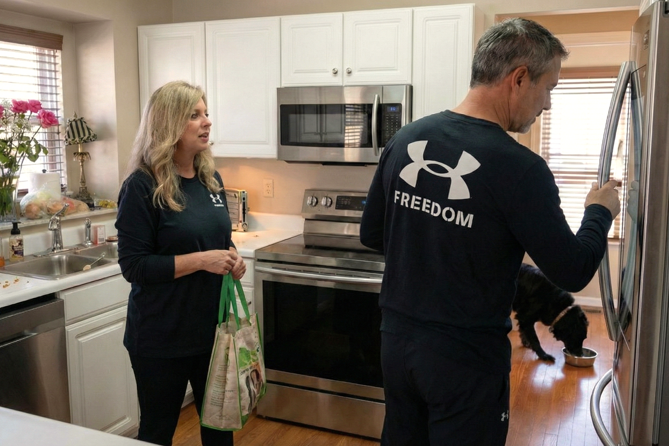 Joey Montes opening the refrigerator wearing a Freedom shirt while Heather Killebrew holds a grocery bag in the kitchen.