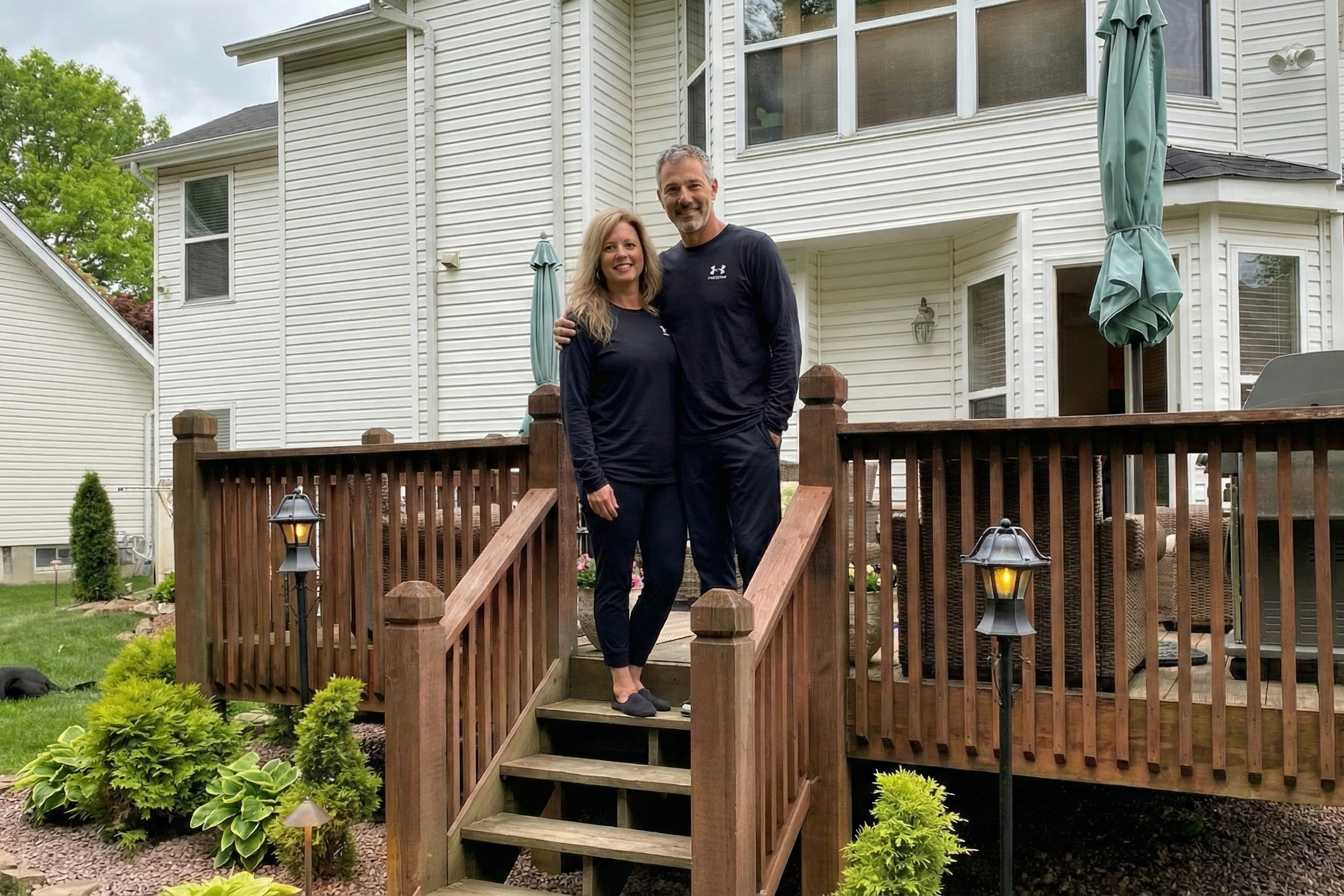 Joey Montes and Heather Killebrew standing together on the wooden deck stairs in their backyard in Wildwood.