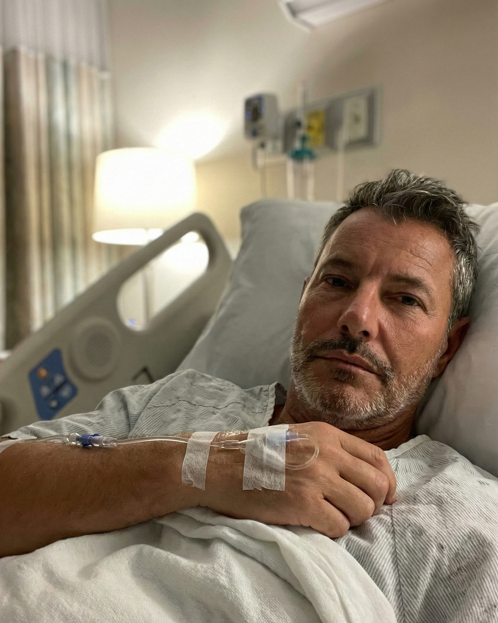 Joey Montes in a hospital gown looking serious and tired, with medical equipment visible in the background.