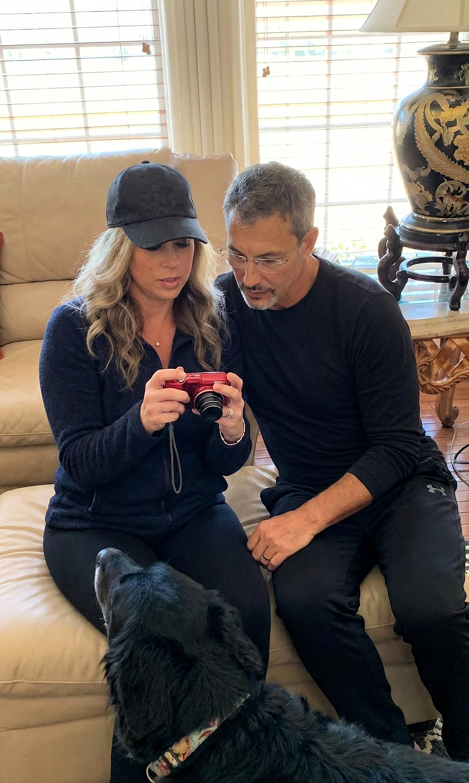 Joey and Heather looking at pictures on a red digital camera, with a black dog in the foreground.