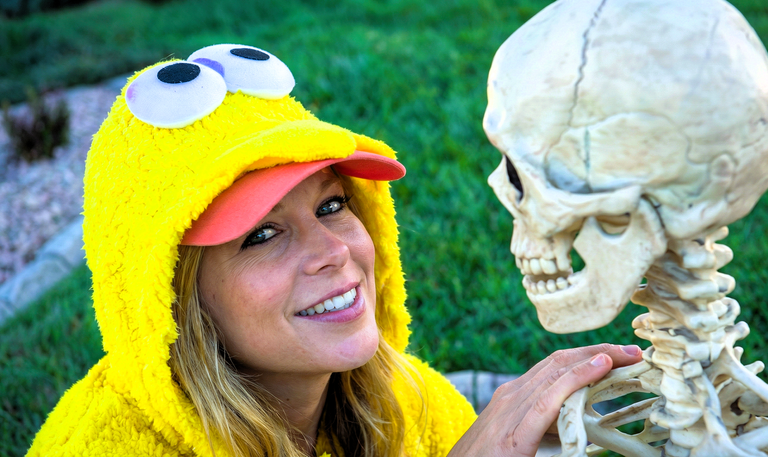 Heather Killebrew in a yellow costume looking lovingly at a plastic skeleton prop.