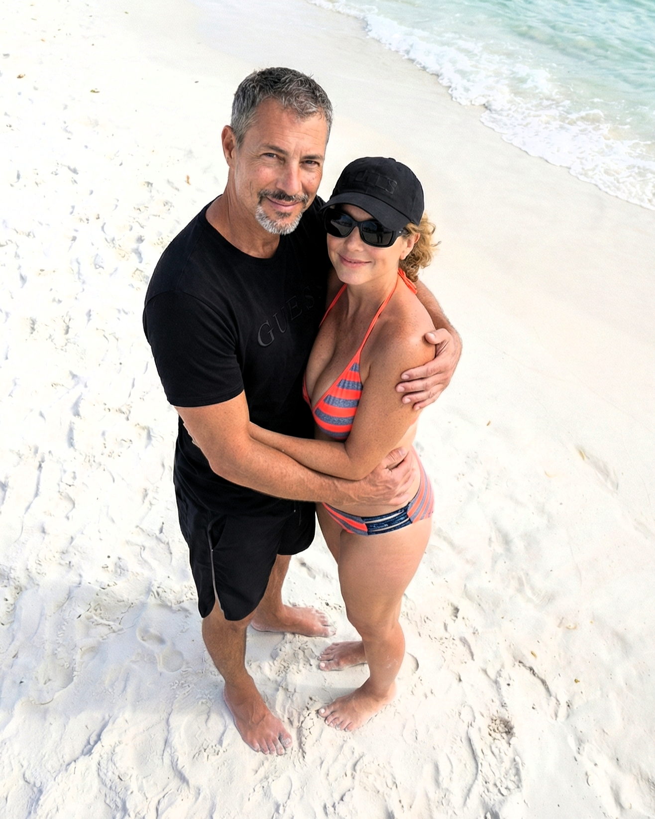 High-angle shot of Joey Montes and Heather Killebrew hugging on the beach, emphasizing the white sand and blue water.