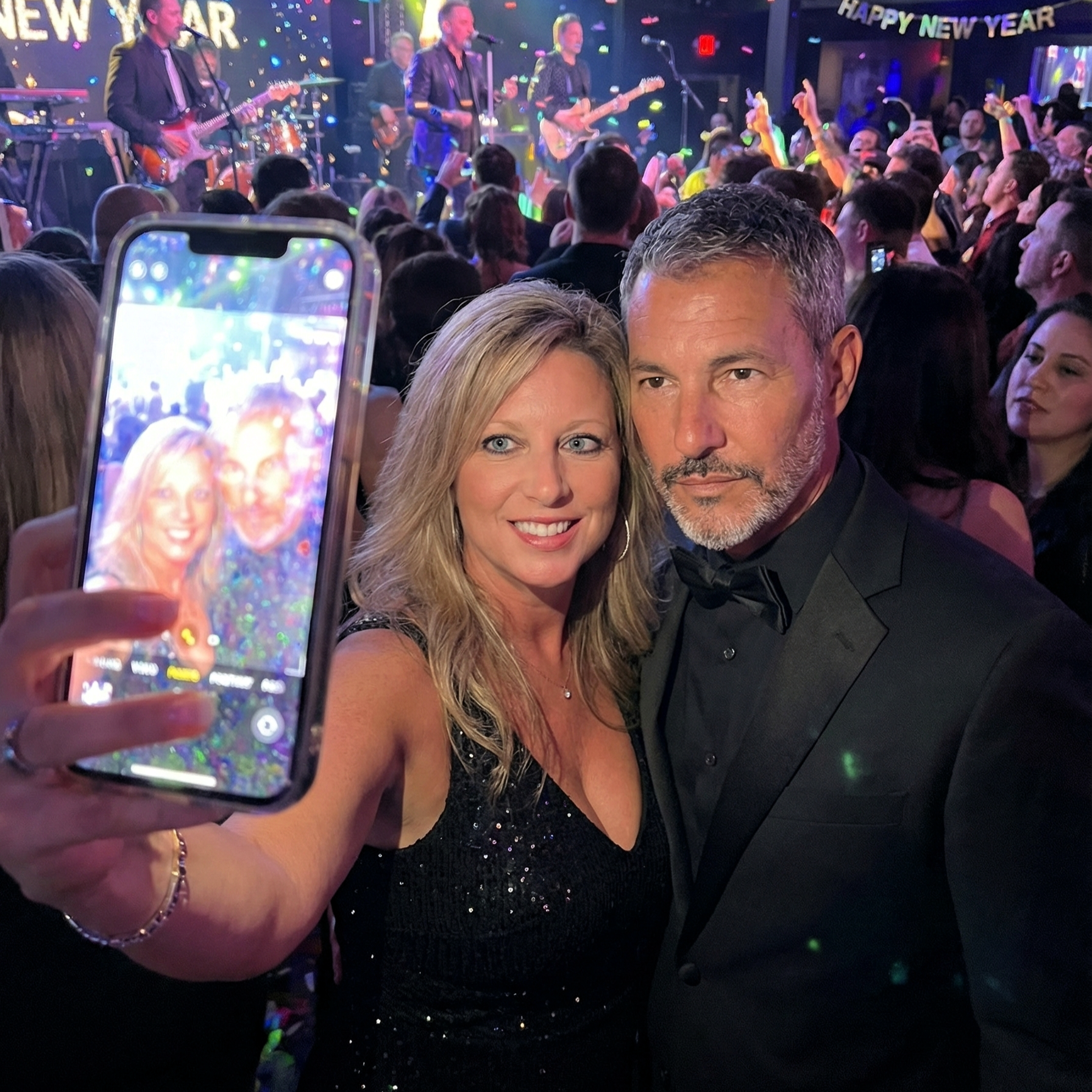 A photo of a smartphone screen capturing a selfie of Heather Killebrew and Joey Montes at a New Year's Eve concert.