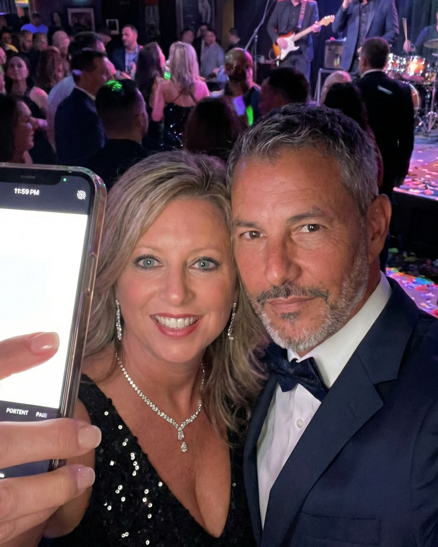 Selfie of Heather Killebrew and Joey Montes at a New Year's Eve party, with the phone screen plainly showing the time 11:59 PM.