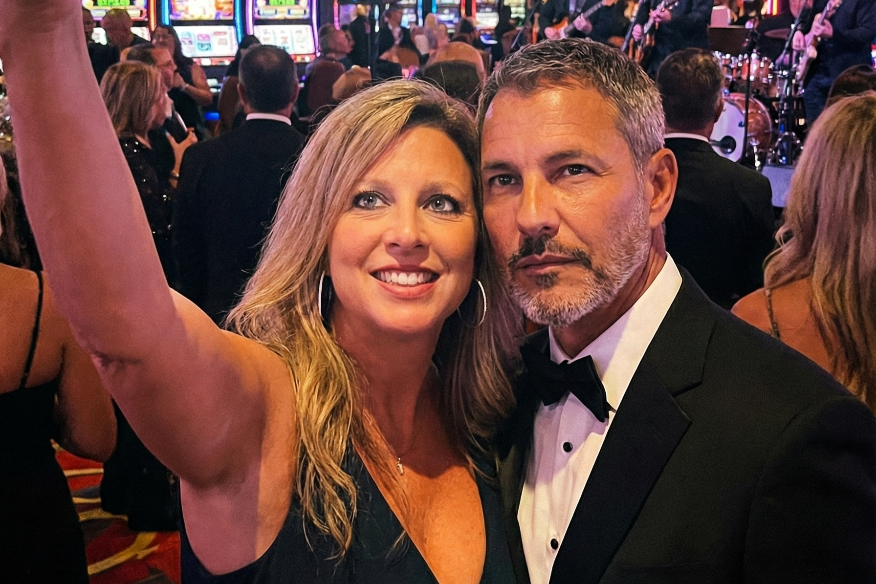 Selfie of Heather Killebrew and Joey Montes in formal black-tie attire standing on a casino floor with slot machines in the background.