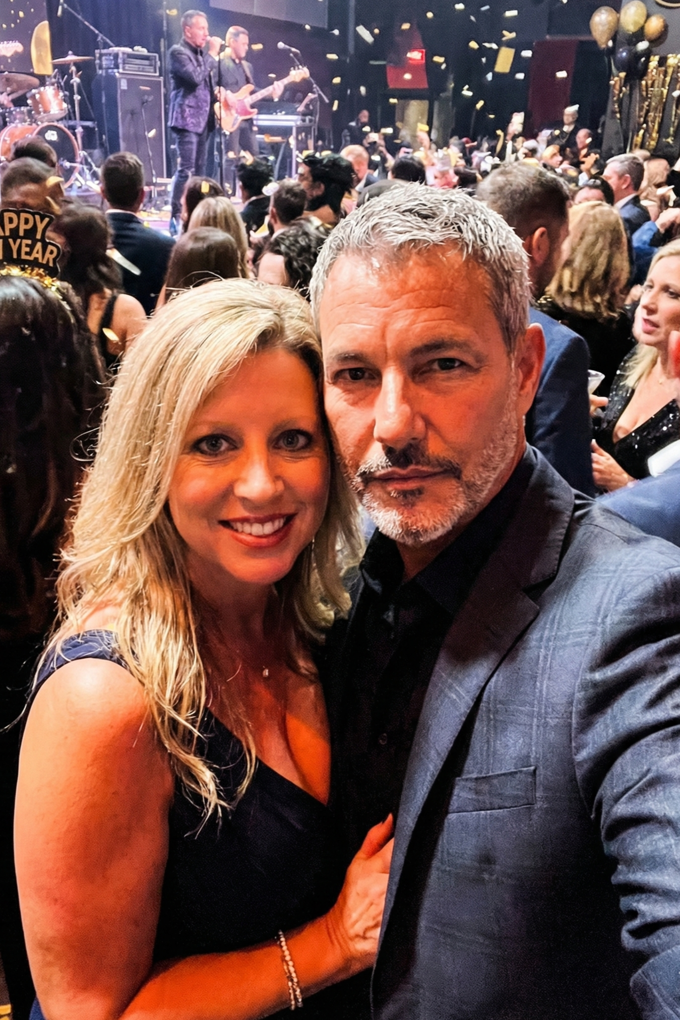 Selfie of Heather Killebrew and Joey Montes at a New Year's Eve party with confetti falling and people celebrating in the background.