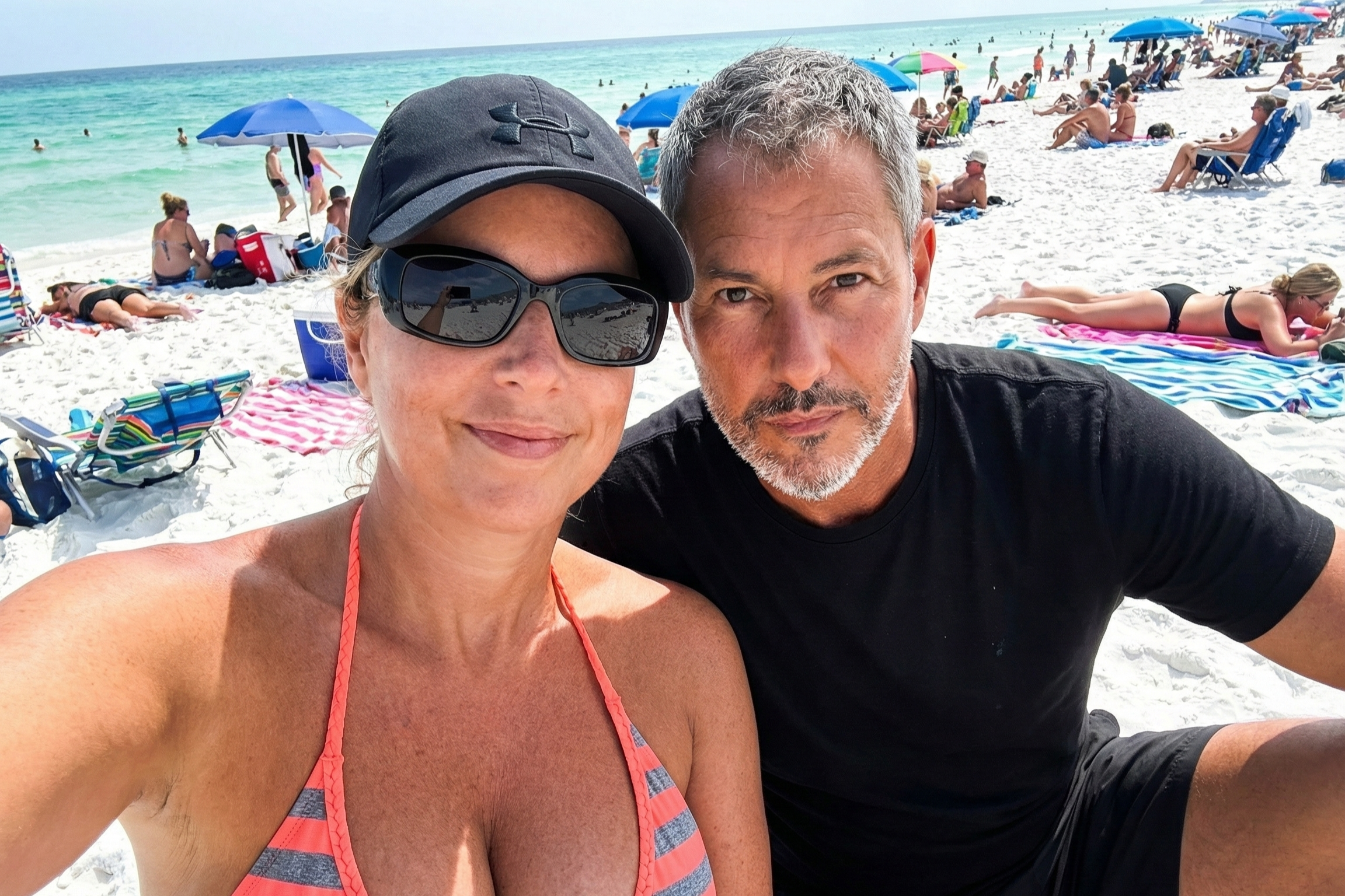 Selfie of Heather Killebrew and Joey Montes (in a black t-shirt) sitting on the white sands of Destin beach.