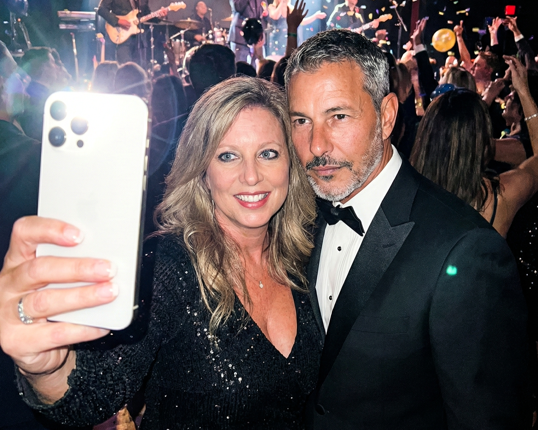 Heather Killebrew taking a selfie with Joey Montes, who is wearing a tuxedo, amidst a crowded New Year's Eve party.