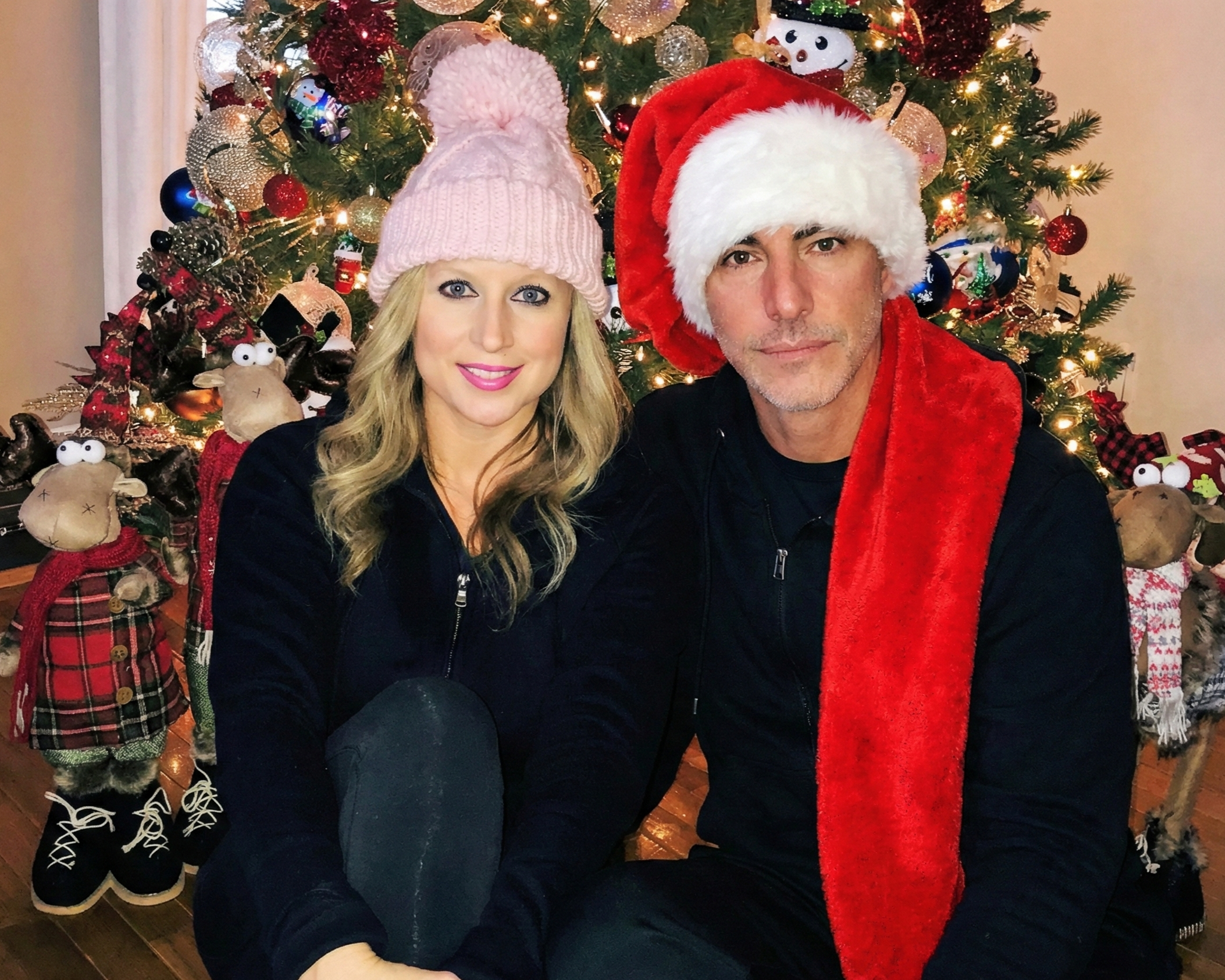 Joey Montes in a Santa hat and Heather in a pink beanie sitting together in front of a Christmas tree in Wildwood, 2018.