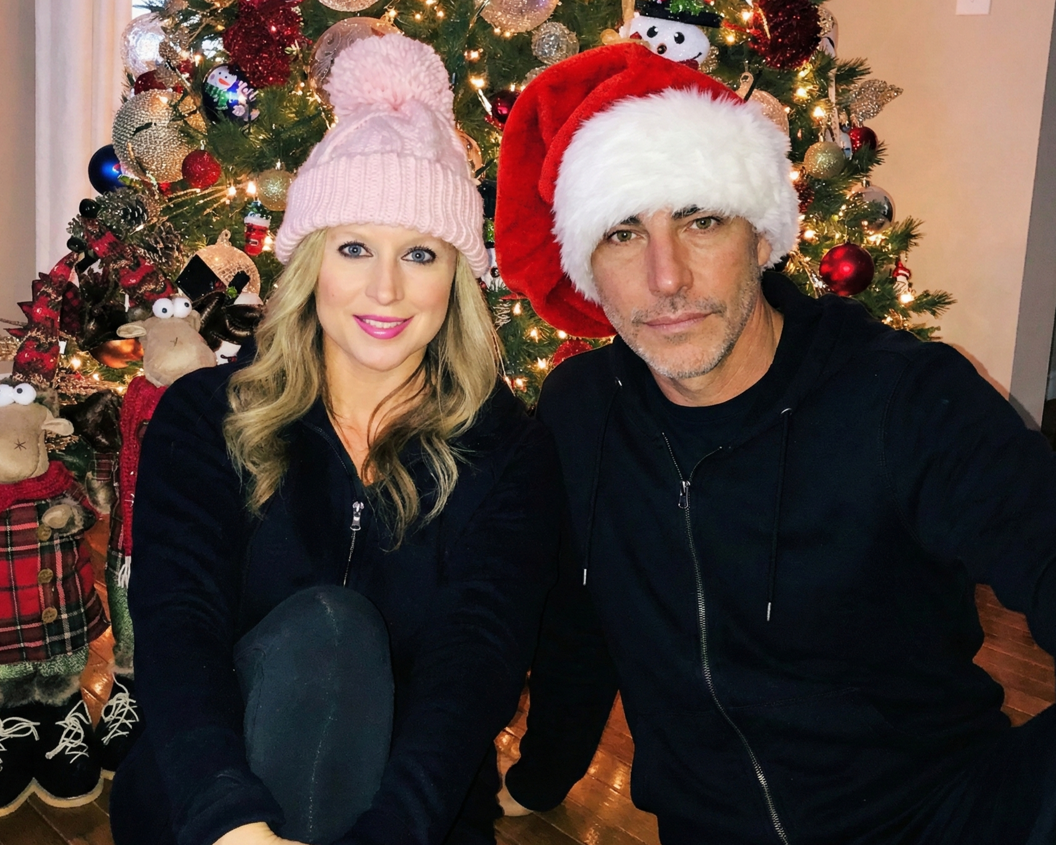 Close-up selfie of Joey Montes in a Santa hat and Heather in a pink beanie by a Christmas tree in Wildwood, 2018.