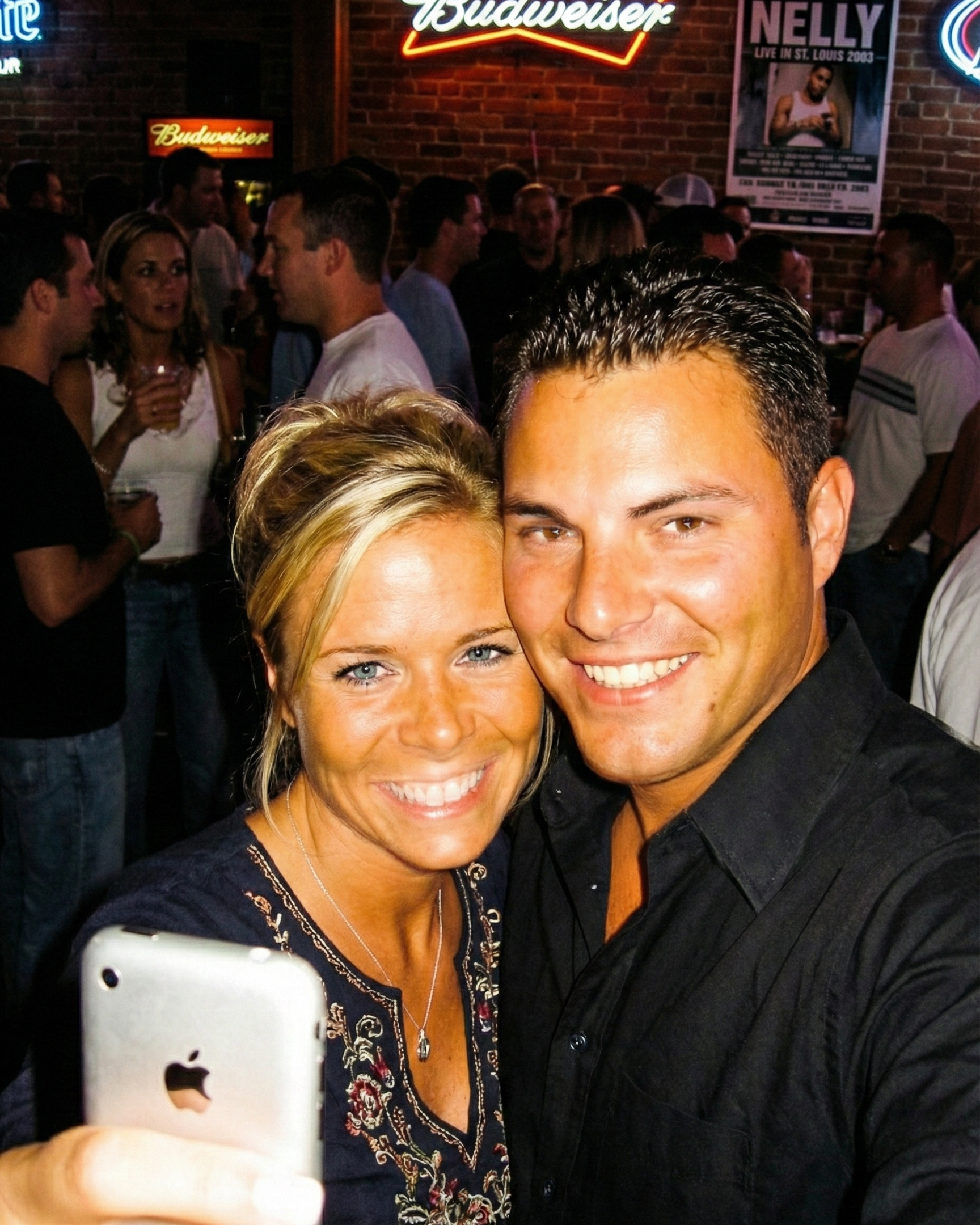 Joey and Dawne taking another selfie at a bar with a Nelly 2003 poster in the background.