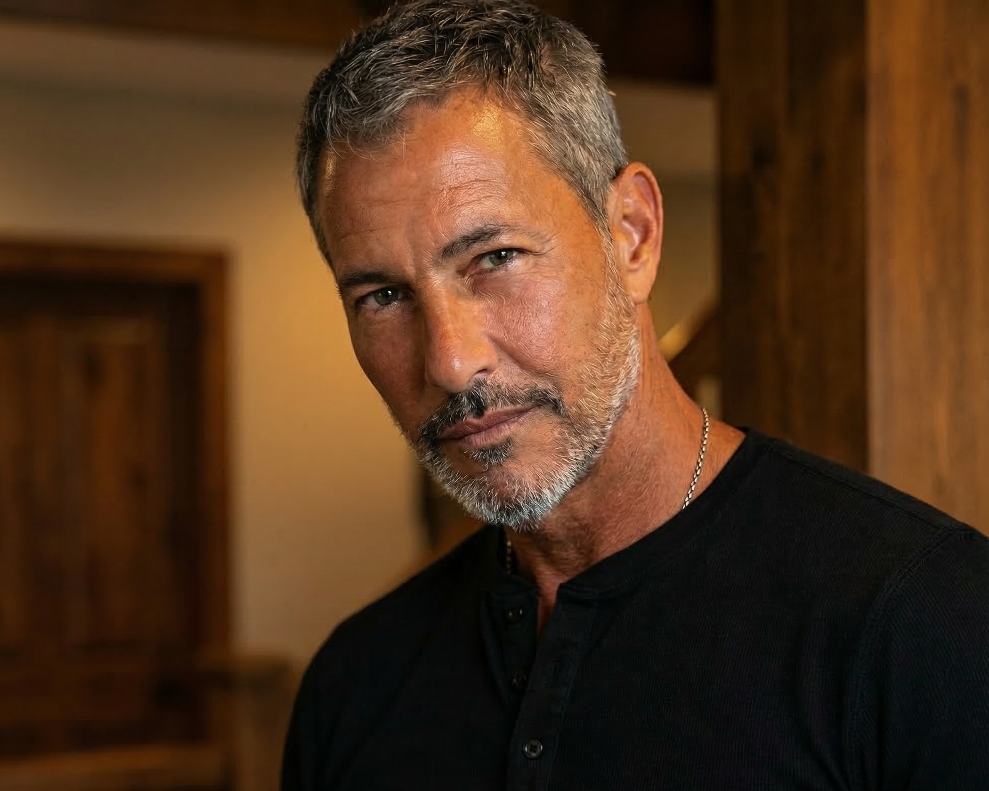 A close-up portrait of a handsome man wearing a black shirt, standing in front of warm wooden doors in Wildwood.