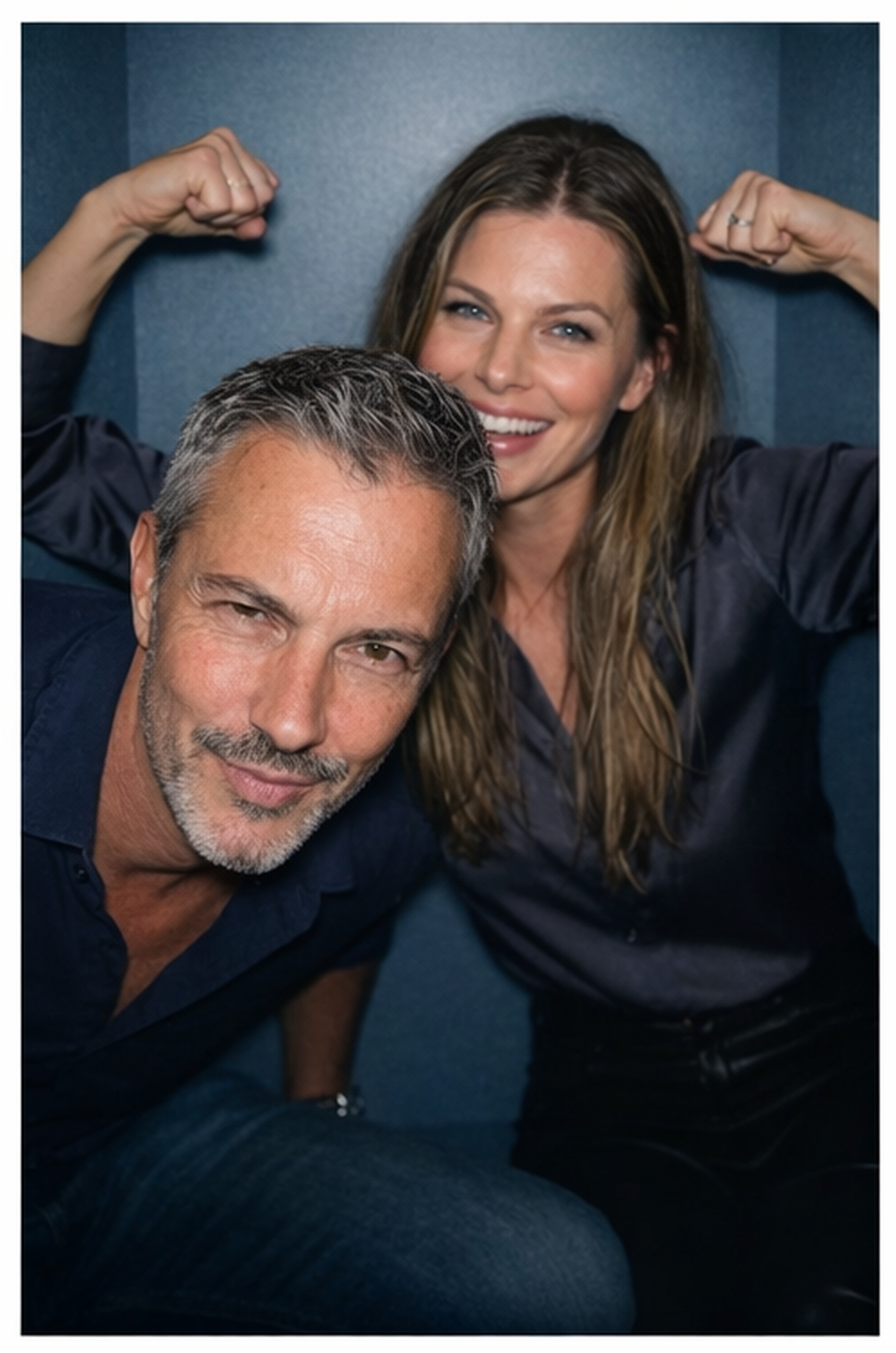 Playful portrait of Joey Montes leaning forward while his female friend flexes her biceps behind him against a blue background.