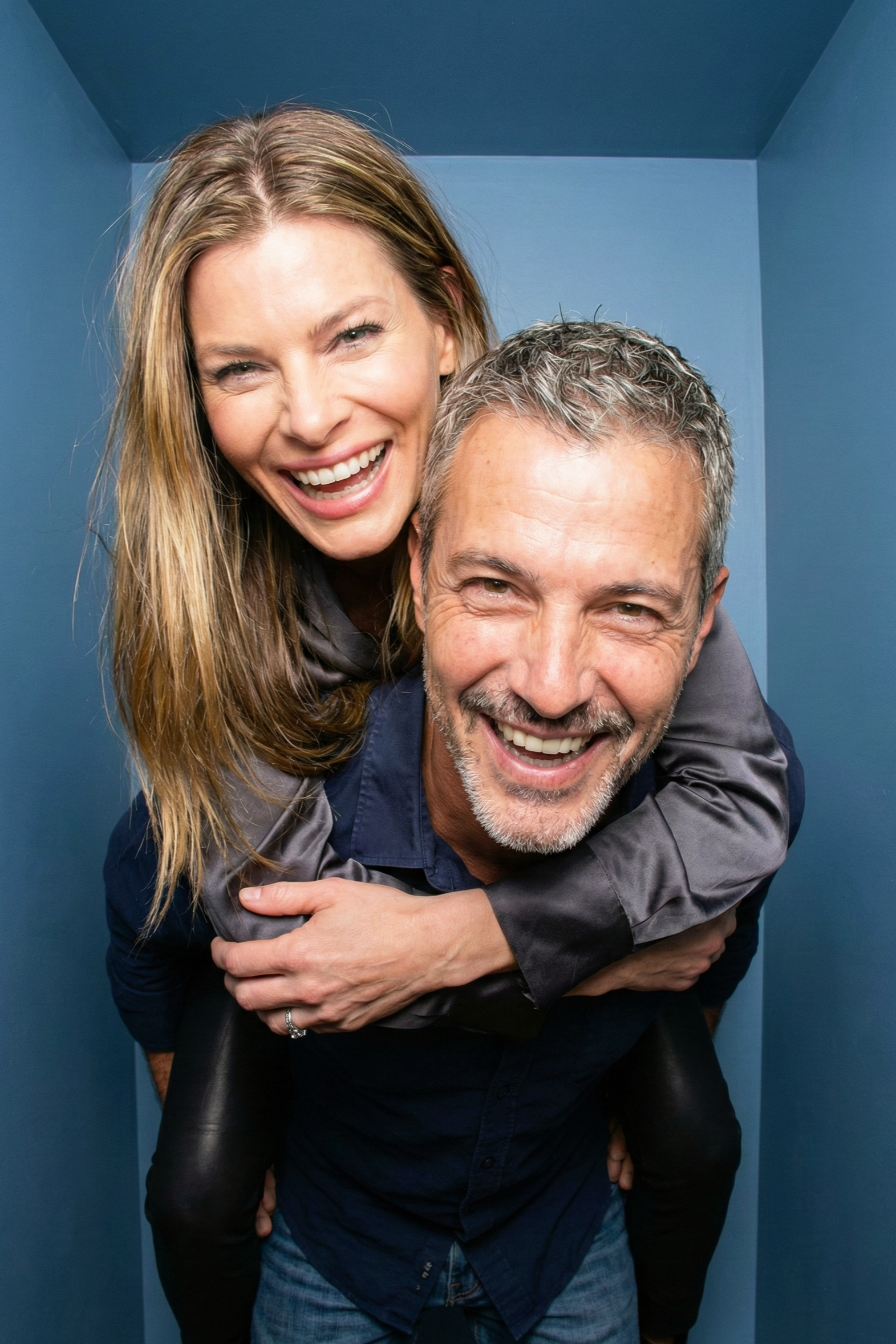 Energetic portrait of Joey Montes giving his friend a piggyback ride, both laughing hysterically against a blue studio background.
