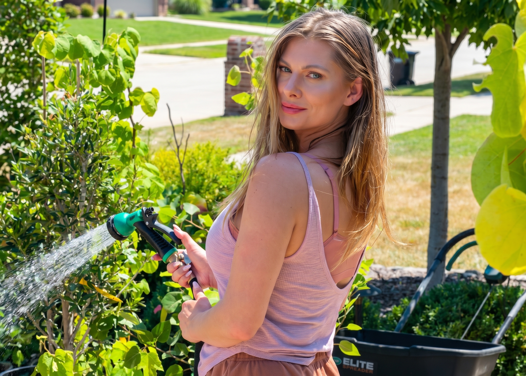 M smiling joyfully while watering potted plants in the driveway during a bright July afternoon.